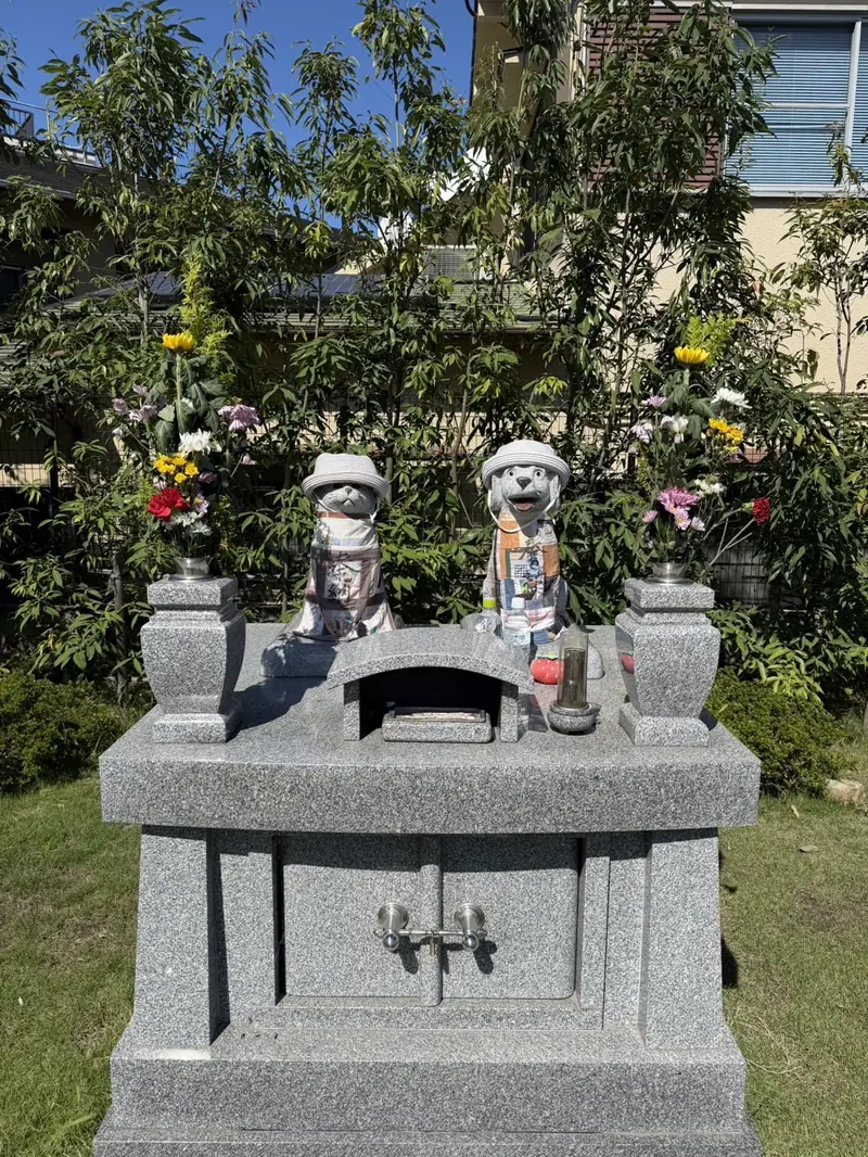 ペット供養塔。帽子と前掛けをつけた犬と猫の石像、両脇に献花
